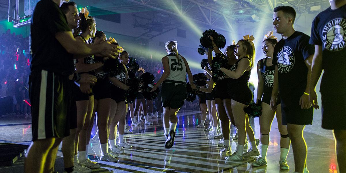 Athletes enter the gym surrounded by cheer leaders and team members